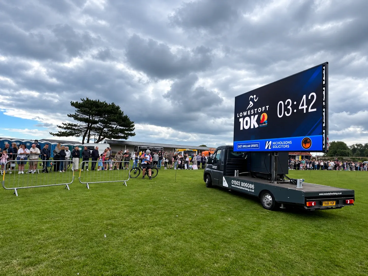 Our digivan parked on the grass beside the finish area, its screen showing a live race clock with the event sponsors underneath